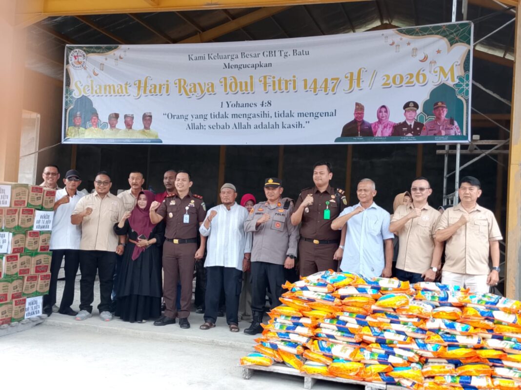 Sekelompok orang yang terdiri dari pengurus GBI Tanjung Batu, aparat kepolisian, kejaksaan, dan tokoh masyarakat berfoto bersama sambil mengepalkan tangan. Di belakang mereka terdapat spanduk ucapan Selamat Idul Fitri 1447 H dari GBI, dan di depan mereka tertumpuk puluhan karung beras serta kardus mi instan untuk bantuan sosial.