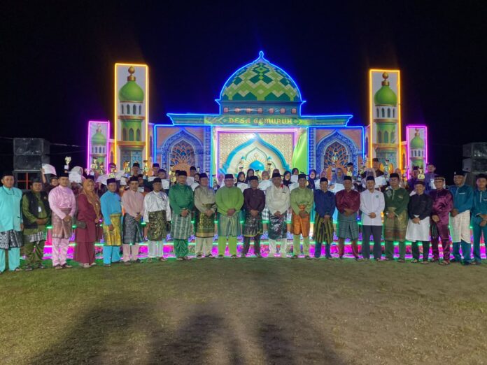 Wakil Bupati Karimun Rocky Bawole bersama panitia, dewan hakim, dan para juara MTQ Tingkat Desa Gemuruh 2026 foto bersama di depan panggung utama saat malam penutupan.