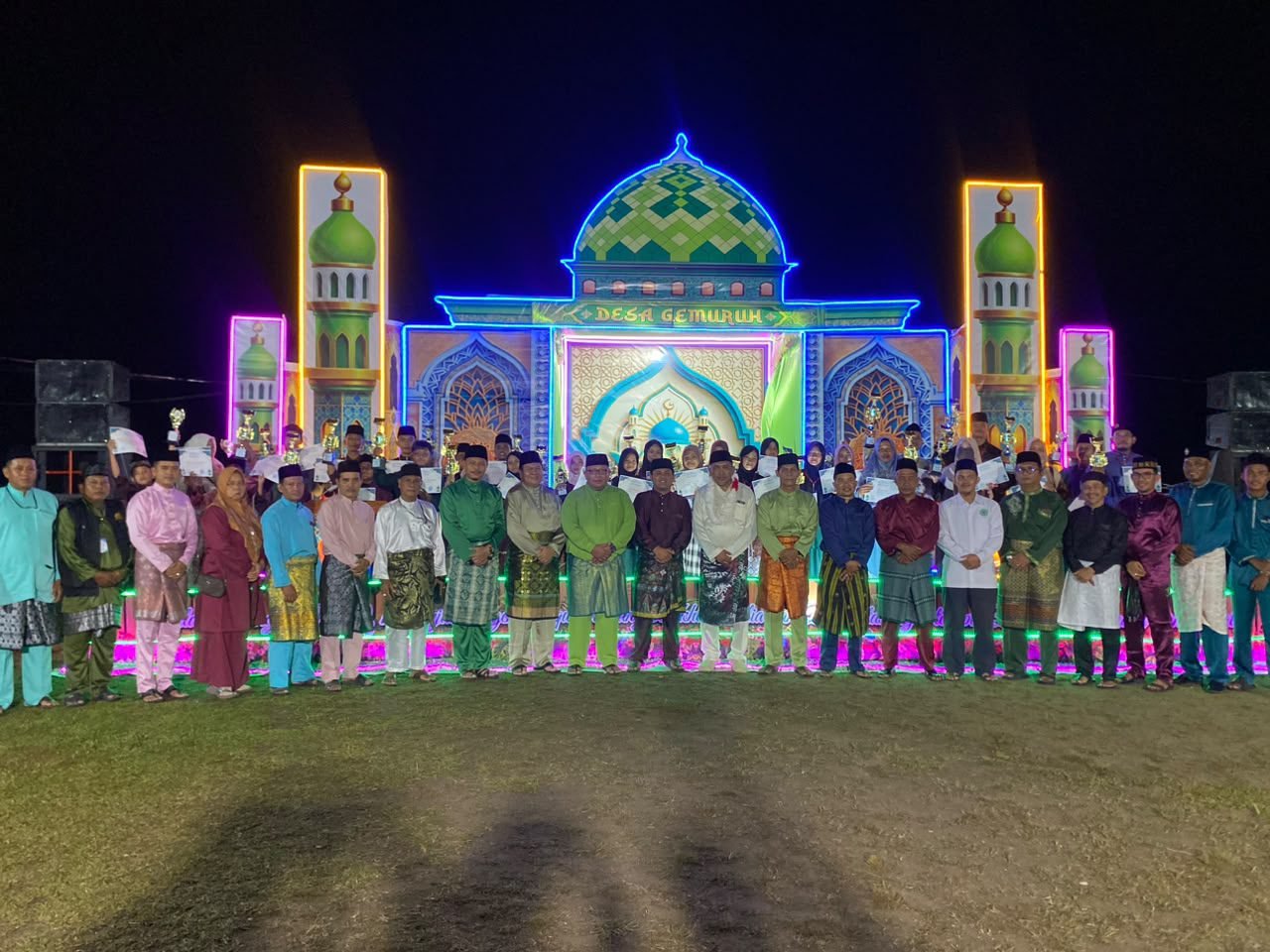 Wakil Bupati Karimun Rocky Bawole bersama panitia, dewan hakim, dan para juara MTQ Tingkat Desa Gemuruh 2026 foto bersama di depan panggung utama saat malam penutupan.